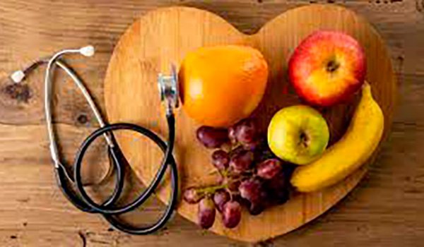 Imagen de una tabla de madera con forma de corazón que posee frutas encima y un estetoscopio apoyado sobre una de éstas.