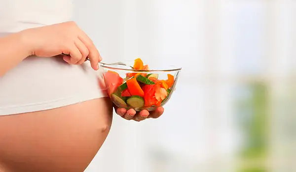 Mujer embarazada con un recipiente de frutas.